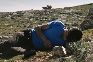 man reclines on a rock hill with a tank in the background