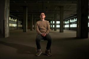 an asian man sits in the middle of an abandoned warehouse 