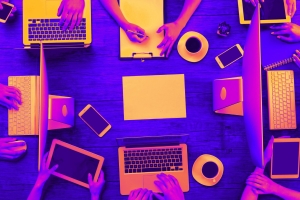 A neon-colored stock image of a table full of people working on computers and laptops.