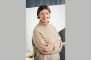 A light-skinned woman with cropped brown hair and a beige sweater gently smiles at the camera.