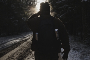 Backlit by the sun, the silhouette of a man walking down a snowy road.