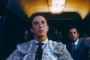 Inside a van, a man in an elaborate bullfighting outfit sits surrounded by his entourage.