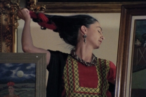 In a reflected mirror, a woman with long black hair removes a red hair ribbon.