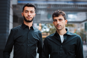 Two men in black button-up shirts look at the camera.