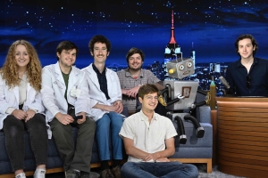 This is a group of friends sitting on a couch and floor at the tonight show. There is also a robot in the photo.