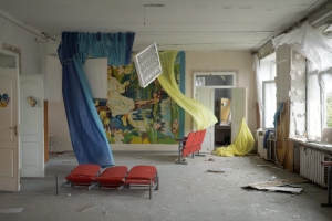 An empty room that has been bombed with fabrics, chairs strewn around and windows open.