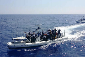 A small boat with around a dozen people motors toward shore.