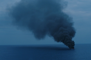 A plume of smoke rises from the ocean surface.