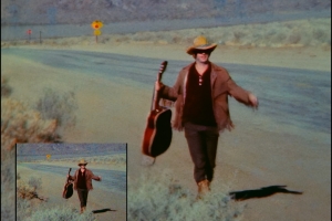 An image is shown twice, once in the bottom left hand corner of the frame and once taking up the frame's entirety. They both picture a man in a cowboy hat with a guitar on a desert road. The larger sized image has been digitally restored, and looks much smoother and cleaner. 