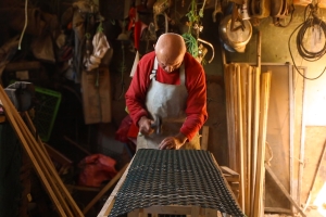 A man in a red shirt beds over a worktable.
