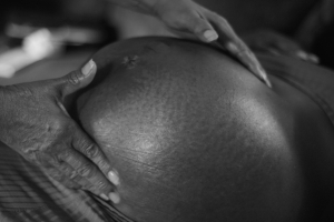 Black and white image of a pregnant woman's belly with the midwive's hand gently holding it.