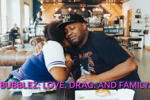 Bubblez and his teenage daughter hug while sitting at a table at a coffee shop.