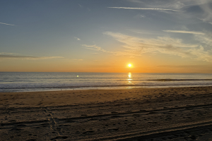 A Malibu beach at sunset with the sun over the ocean and gentle waves along the shore.