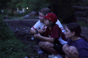 Three children at dusk in the woods crouched down looking into the trees and grass