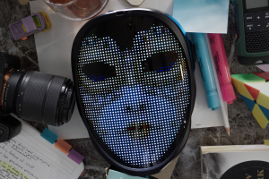 A picture of several items on a table including; A mask that one mom wears in the film, a camera, pens, sticky notes, and several other small items.