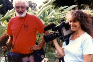 Puhipau, a man holding a mic and wearing headphones, and Joan Lander, a woman holding a camera and smiling, filming in 1989. Courtesy of Joan Lander