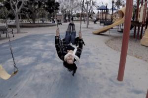 A woman from the film swings on  a swing in the middle of a playground; her head is upside-down as she faces the camera.