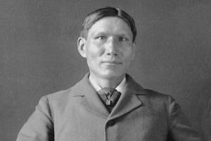 A black and white portrait of an Indigenous man with short hair wearing a suit. 