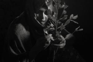 Black and white image of Habu Abdella, a young Ethiopian woman holding a stem of khat leaves. From Jessica Beshir's 'Faya Dayi.' Courtesy of Feyatey LLC