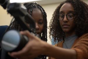 Two Black women students look into a video camera screen. Photo credits Marco Marco Poggio.