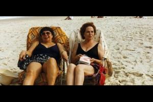 Two older women smile while sitting in beach chairs near the ocean, from Heddy Honigmann's 'Amor Natural'.
