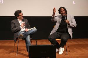 Ben Mankiewicz is a white male TV personality in conversation with Roger Ross Williams, a Black male filmmaker during IDA's Conversation Series, in 2016. Image courtesy of Conversa. 