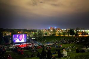 An outdoor nighttime screening: the audience sits on a grassy hill