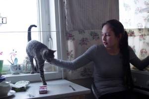 Kirsten Kleist Petersen is a young woman wearing a gray shirt. She is sitting on a chair by a window and petting her cat. From Sidse Torstholm Larsen and Sturla Pilskog’s ‘Winter’s Yearning.’ Courtesy of 'POV.' 