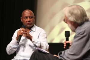 Raoul Peck speaking into the mic facing with Kenneth Turan