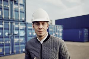 A port worker standing in front of several blue ship crates.