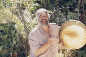 Bruce stands holding a drum before a forest.