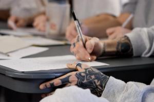 the tattooed hands of an inmate fill out paperwork.