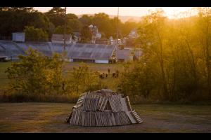 a pile of woodpallets sits on a hill above a pop-warner football practice at sunset.