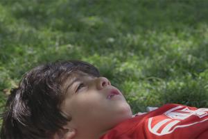 Young Iranian boy lays on the grass looking up at the sky.