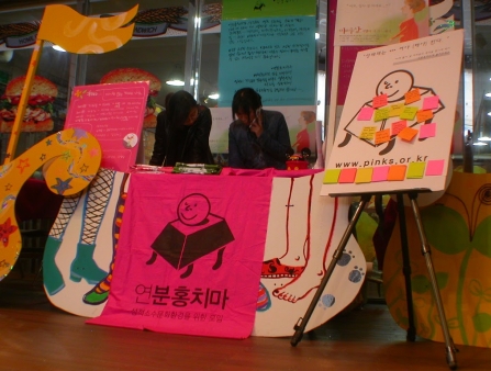 A table with colorful posters and post-it notes, staffed by two women.