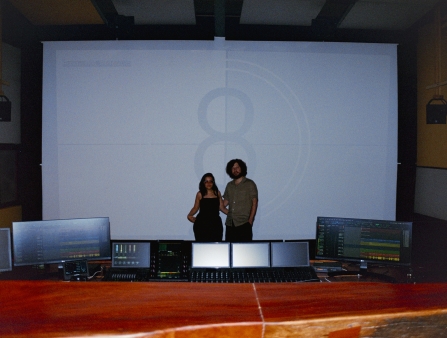 Two people in casual clothes stand in front of a screen.