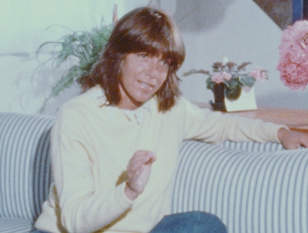A woman with brown bangs sits on a blue and white striped couch.