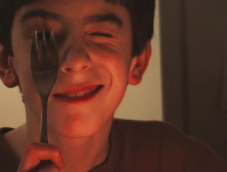 A young person holds a fork over his eye.