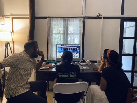 Seen from behind, one man and two men sit staring at a computer screen in an office-like room