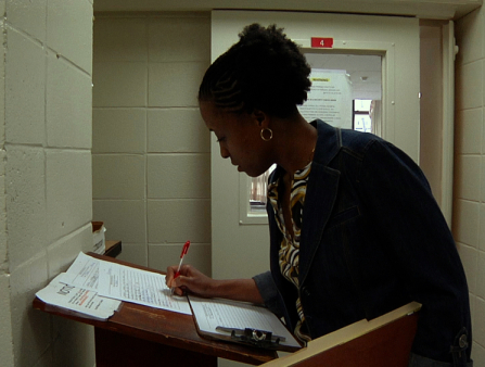 A Black woman signs in in a white hallway.