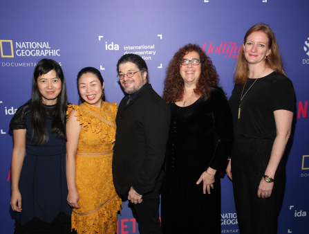 Five smiling filmmakers stand in front of an IDA step and repeat.