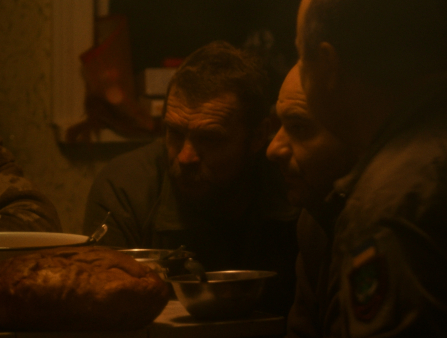 Dimly-lit shot of three soldiers gathered at a dinner table
