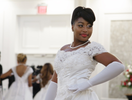 A young Black woman in a debutante's white dress poses in a ballroom.