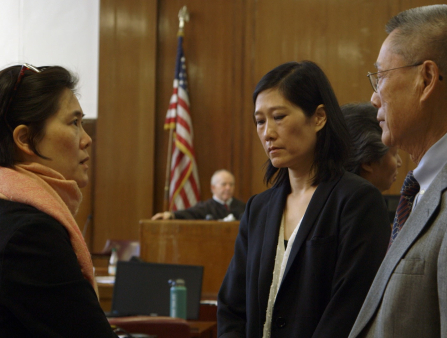 In a courtroom, a father and his two daughters talk solemnly.