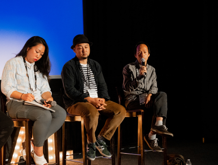 Three people sitting on stools in front of a blue screen.