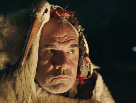 A close up of a stork and a man sidled up to one another at night.