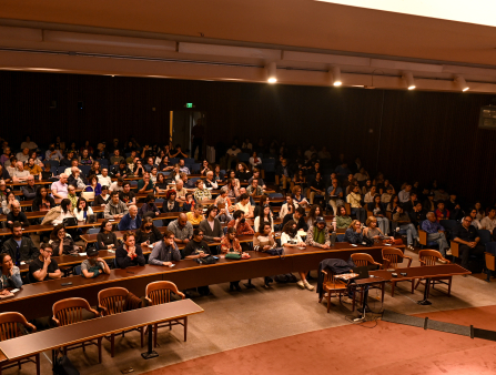 In a lecture hall, an audience of students watches a film.