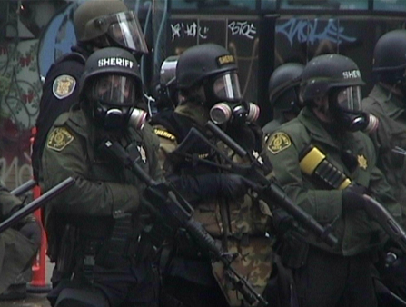 Grainy shot of group of policemen in full riot gear, holding guns.