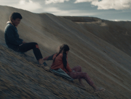Two kids slide down a barren-looking mountain