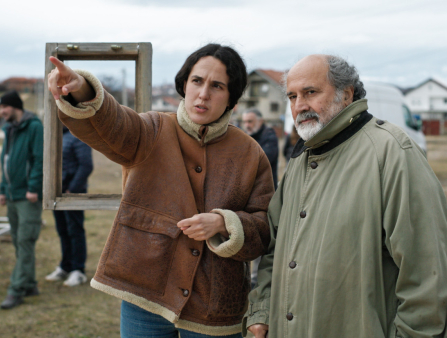 A woman with dark hair tucked behind her wearing a cozy winter jacket points her finger ahead as a balding man with a beard stands next to her